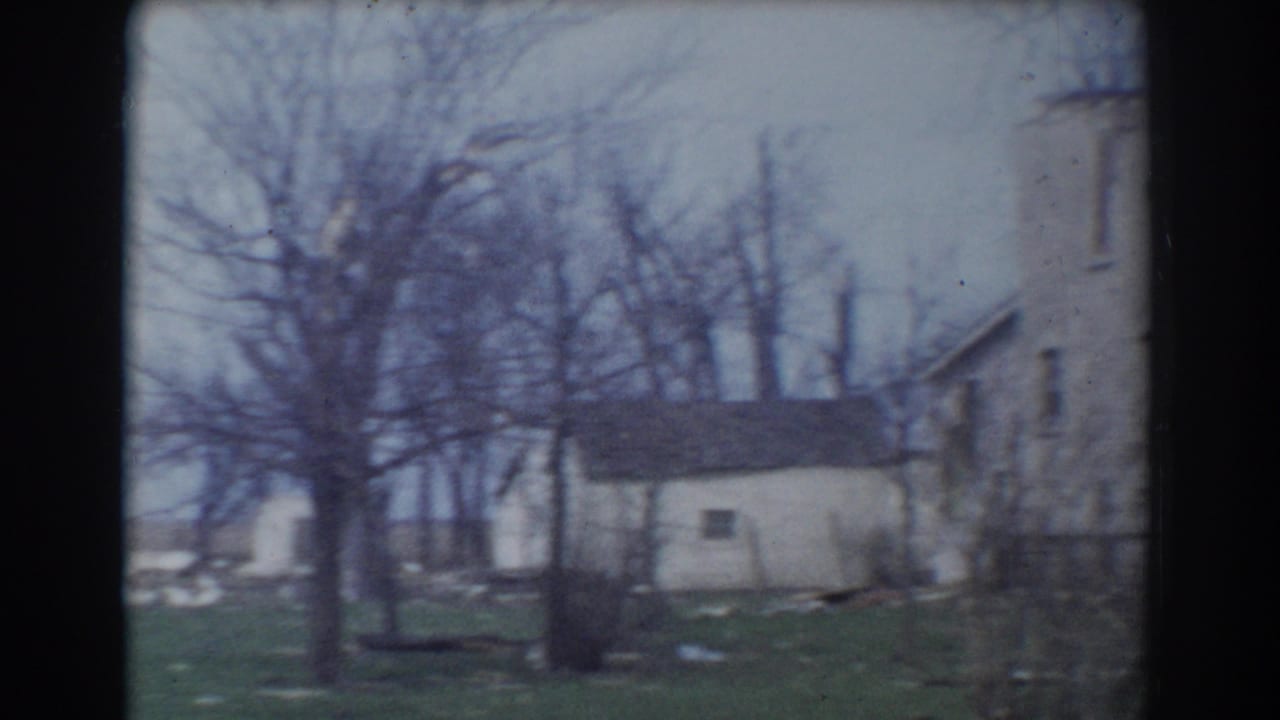 White outbuilding and bare trees near the side of a larger house.