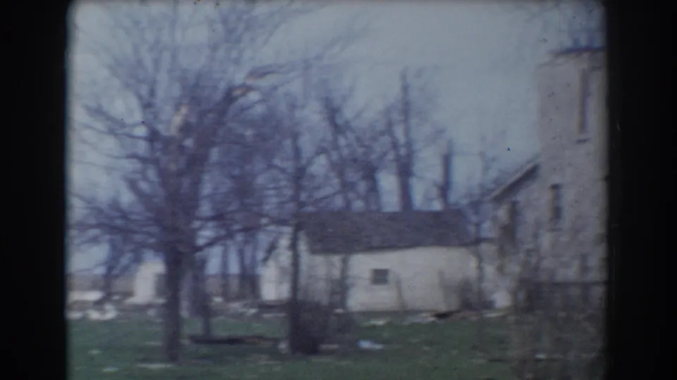 1958 York, Nebraska home-movie frame with a white outbuilding, leafless trees, grass, and part of a weathered house exterior.