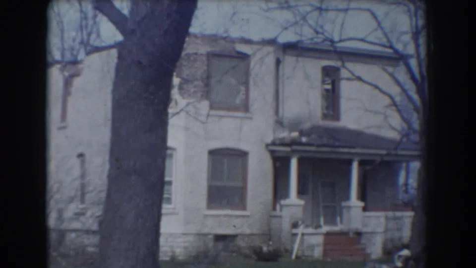 1958 York, Nebraska 8mm frame showing an older house with porch steps, dark windows, bare trees, and a large foreground tree.
