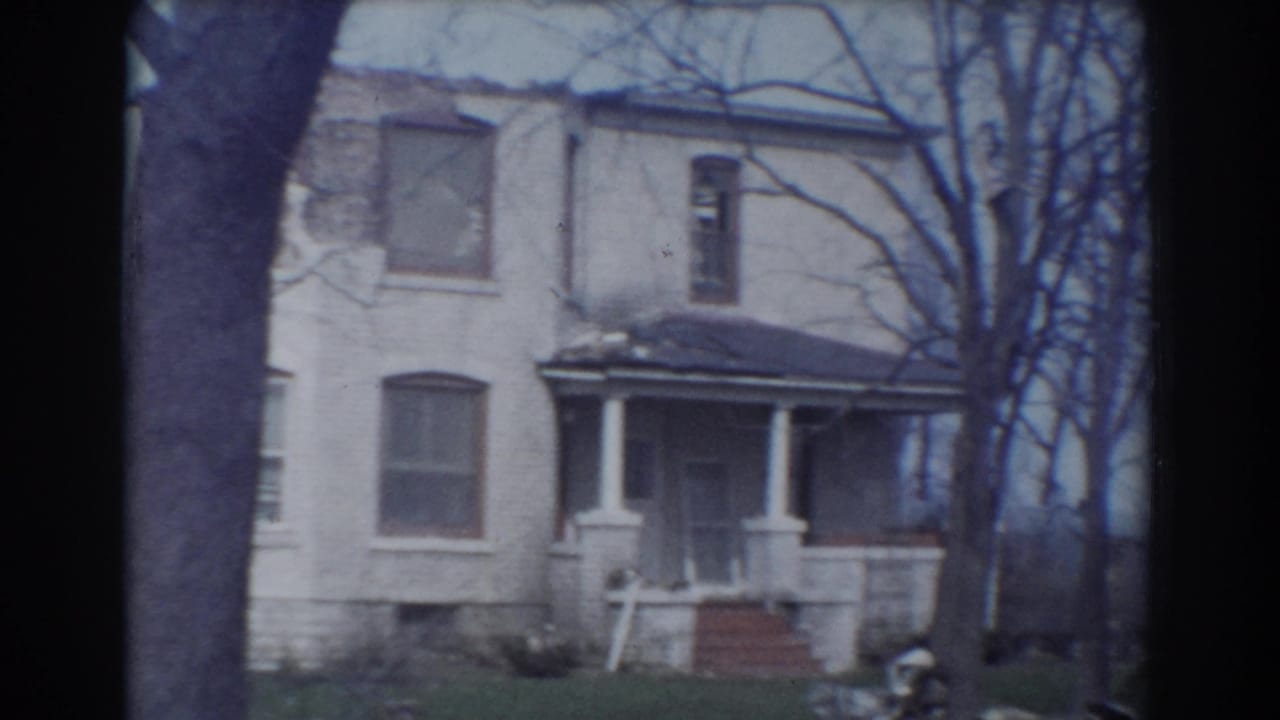 Weathered two-story house with porch columns, bare trees, and grass in front.