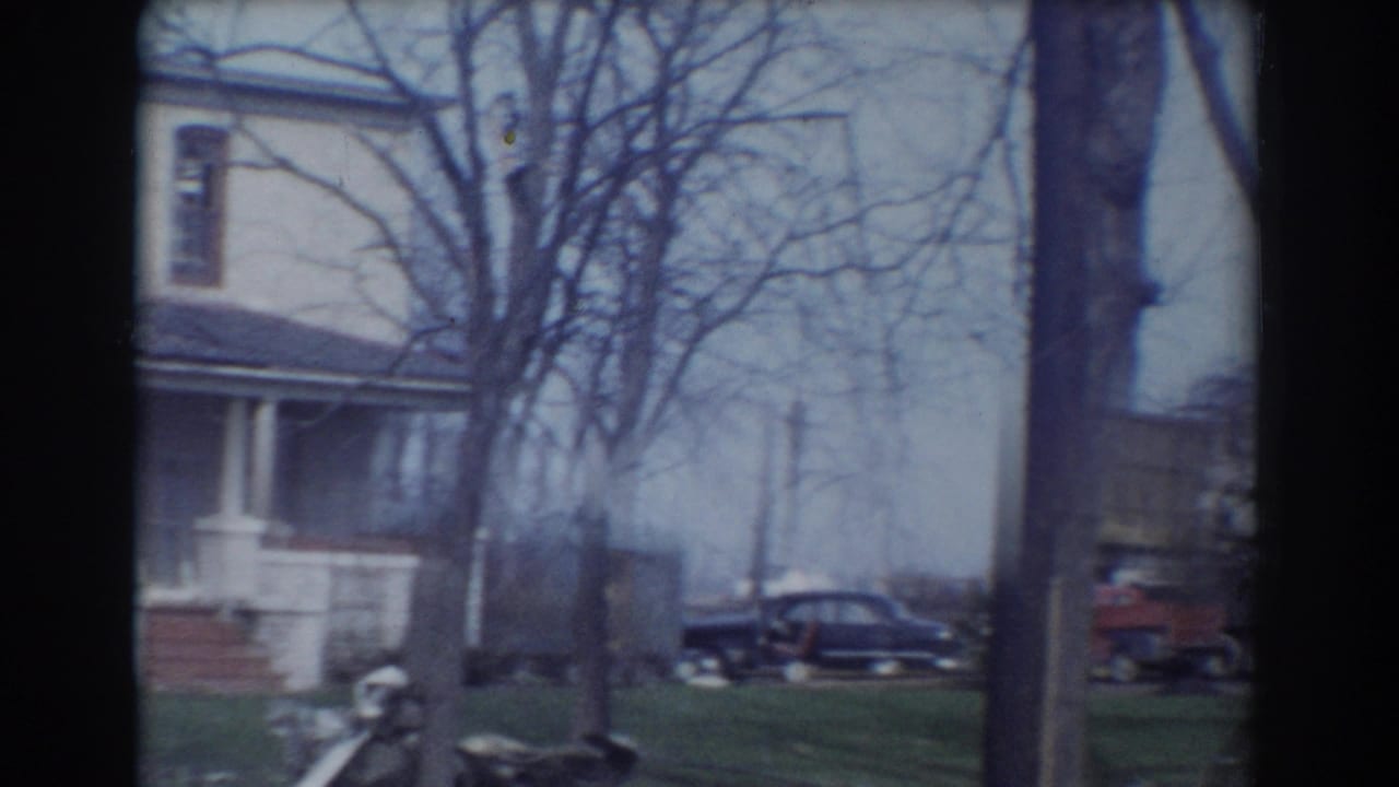 House porch and yard with bare trees, a dark sedan, and a red vehicle nearby.