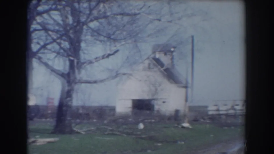 York, Nebraska farmyard view with a white building, leafless trees, fence line, open grass, and scattered debris in 1958 home-movie footage.
