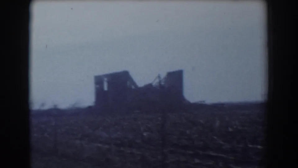 A dark damaged outbuilding or structure stands in an open rural field, with a broken roofline visible in the 1958 York, Nebraska footage.