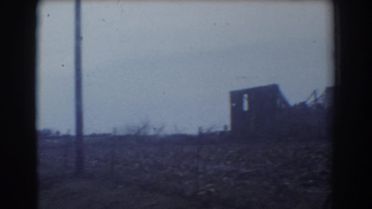 Damaged building beside open rural land seen through a dark 8mm frame edge.