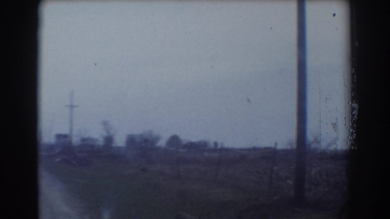 Rural road view with utility pole, fields, and distant roadside forms.