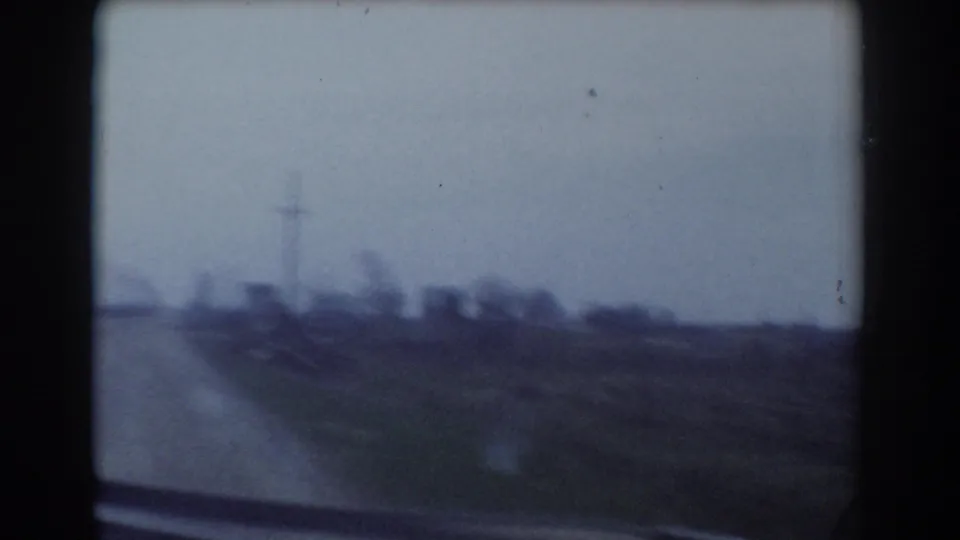 Soft 8mm road view in York, Nebraska, with open fields, a pale sky, and distant utility infrastructure.
