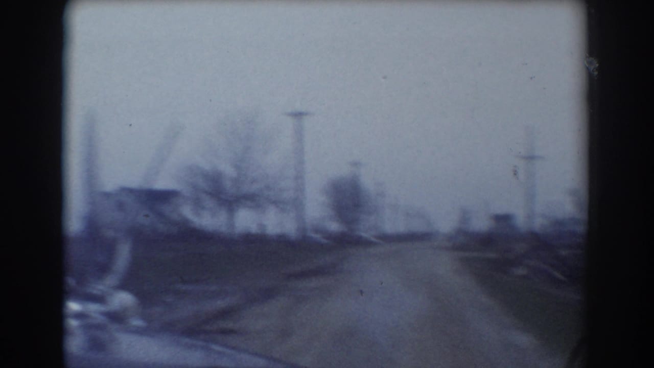 Rural road seen through a car windshield with utility poles and houses in the distance.