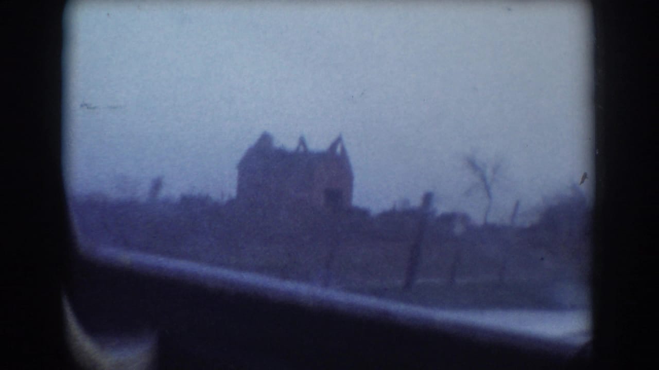 1958 York, Nebraska home-movie frame showing a distant, blurry house beyond a car window and roadside ground.