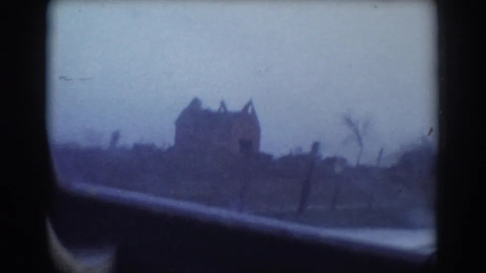 1958 York, Nebraska home-movie frame showing a distant, blurry house beyond a car window and roadside ground.