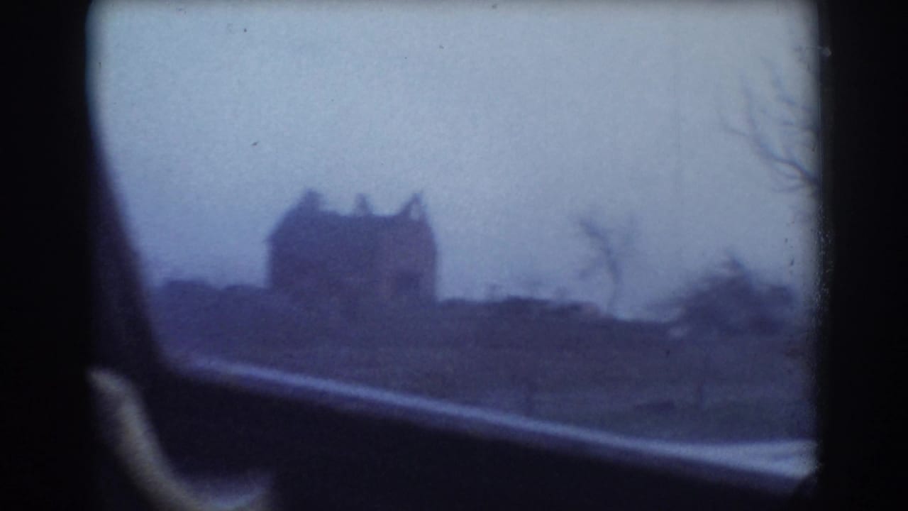 Distant house silhouette and bare trees viewed from inside a moving car.