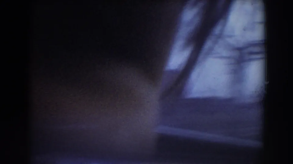 A heavily blurred home-movie frame from the York, Nebraska drive-by, with car interior darkness, bare branches, and roadside forms.