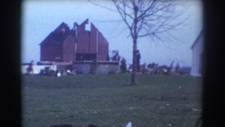 York, Nebraska 1958 frame showing a damaged red rural building, a bare tree, debris, and people near the site.