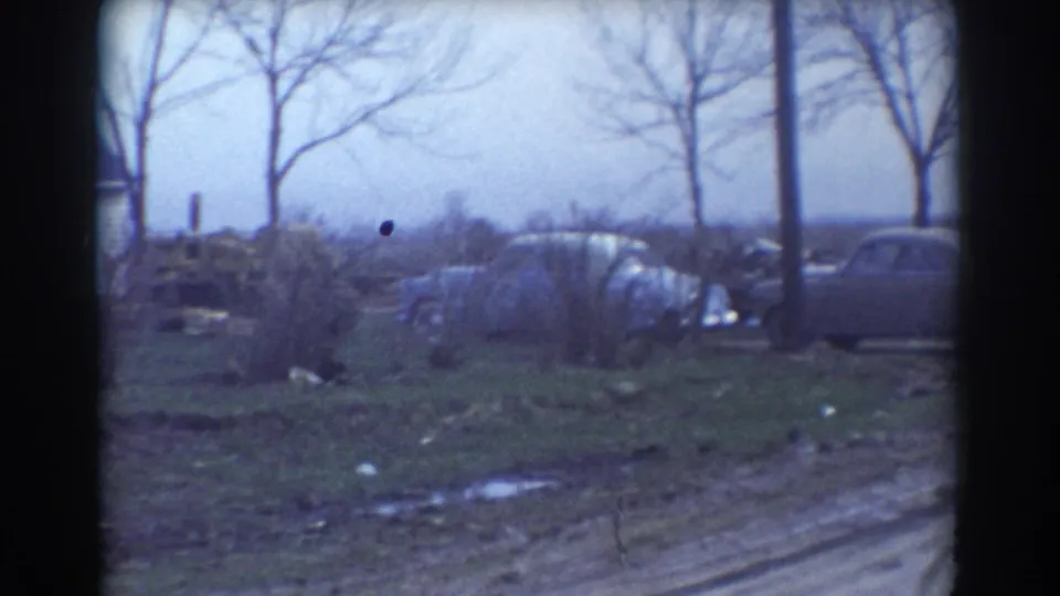 1958 York, Nebraska 8mm view of a muddy roadside with bare trees, a utility pole, brush, and a pale parked car partly visible.
