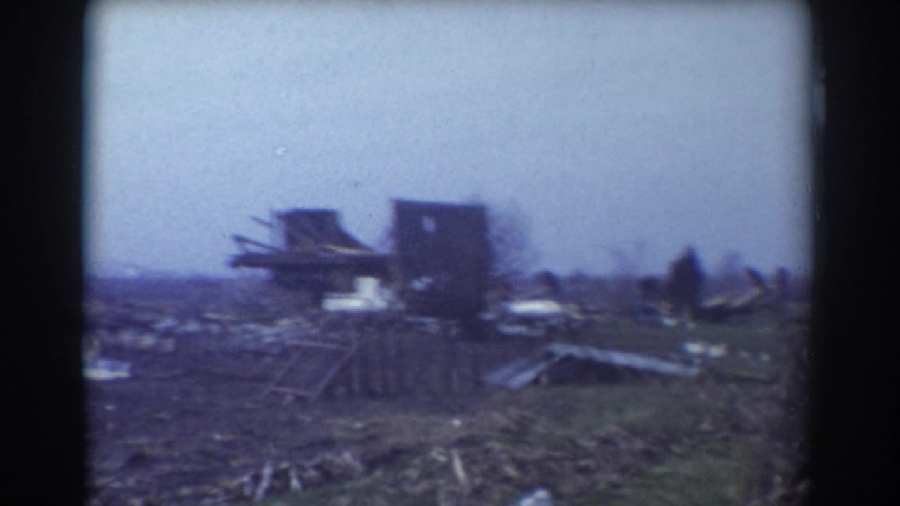 1958 York, Nebraska home-movie frame showing scattered storm debris, damaged farm structures, and open field under a pale sky.