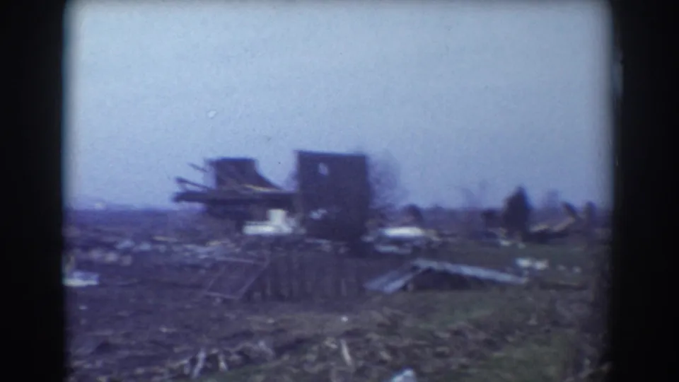 1958 York, Nebraska home-movie frame showing scattered storm debris, damaged farm structures, and open field under a pale sky.