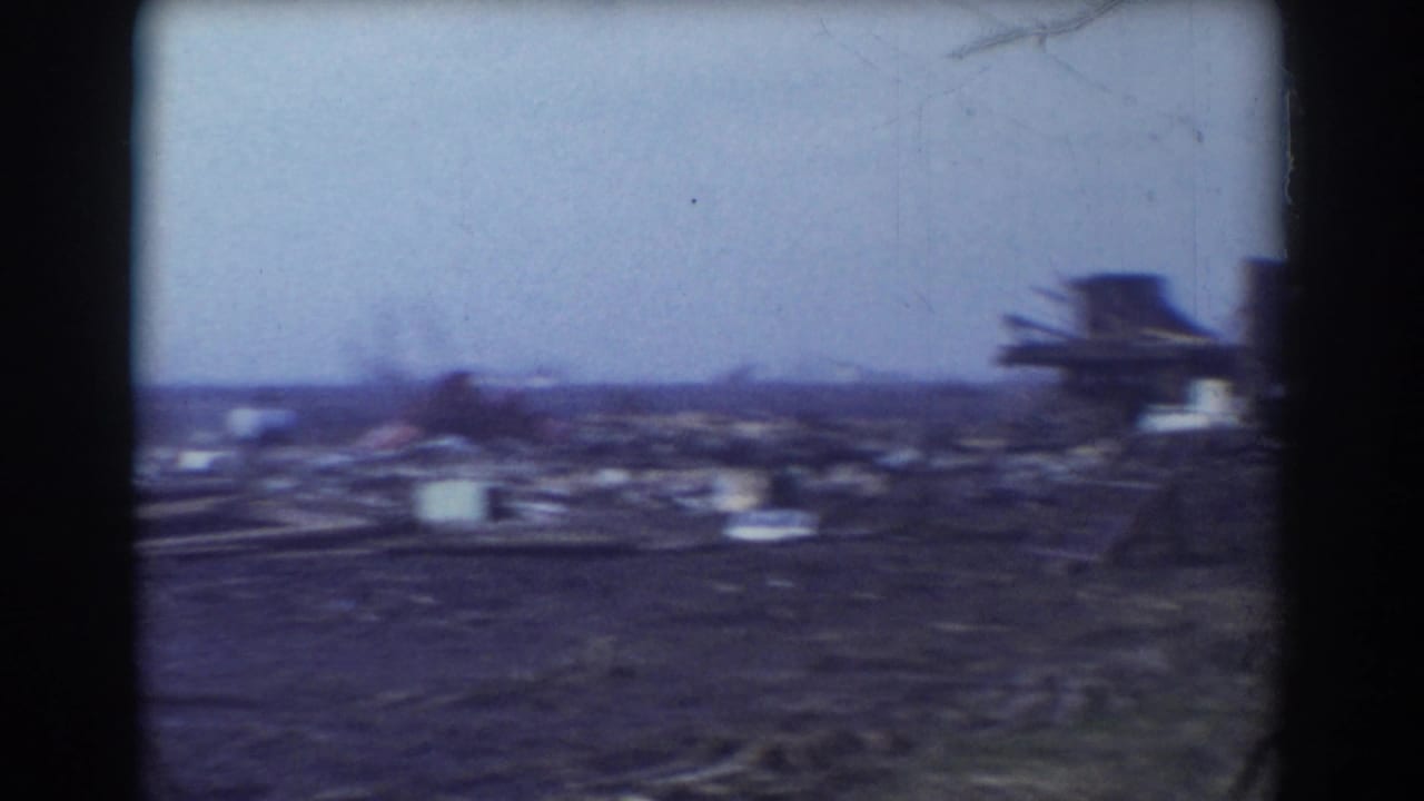 Debris-strewn farm field with a damaged structure near the right edge.