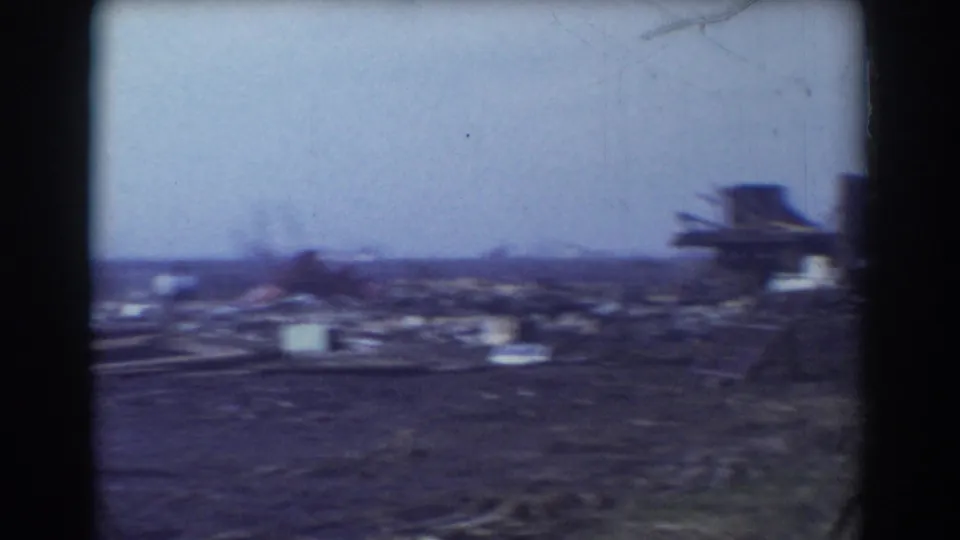 Rural York, Nebraska storm aftermath view with scattered debris across a field and a damaged farm structure at the edge of frame.