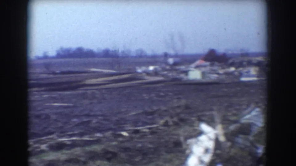 1958 York, Nebraska home-movie frame showing a muddy debris-strewn field with distant structures after storm damage.
