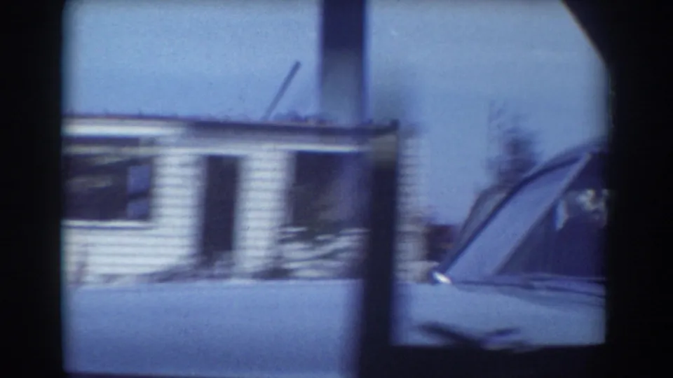 Moving 8mm view of a damaged York, Nebraska house, with a car body crossing the lower frame and storm debris nearby.