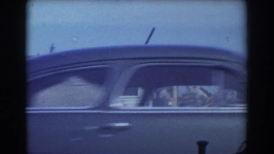 Close 1958-era view of a dark rounded automobile passing the camera during the York, Nebraska storm-damage survey.