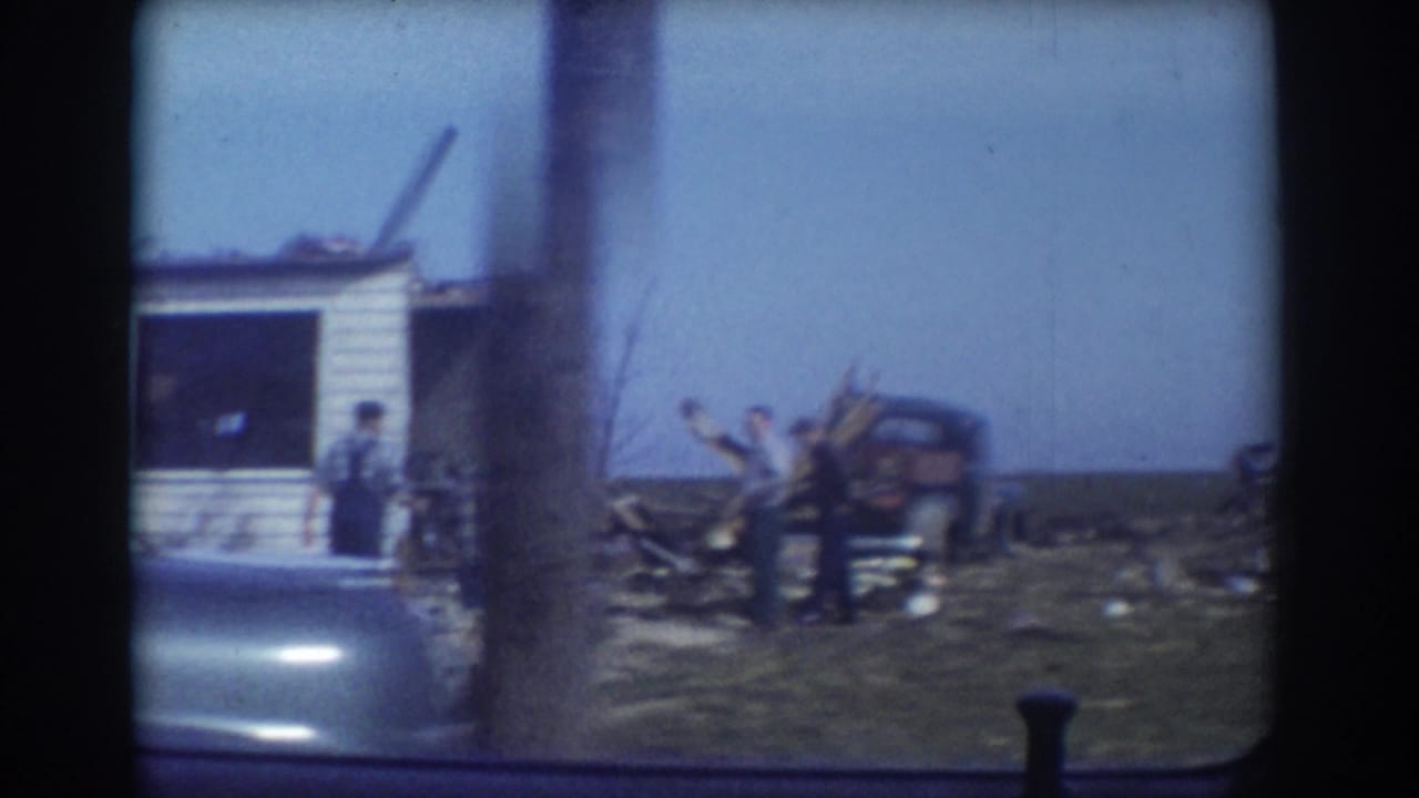 1958 York, Nebraska 8mm frame showing adults near a storm-damaged small building and scattered debris, filmed from inside a vehicle.