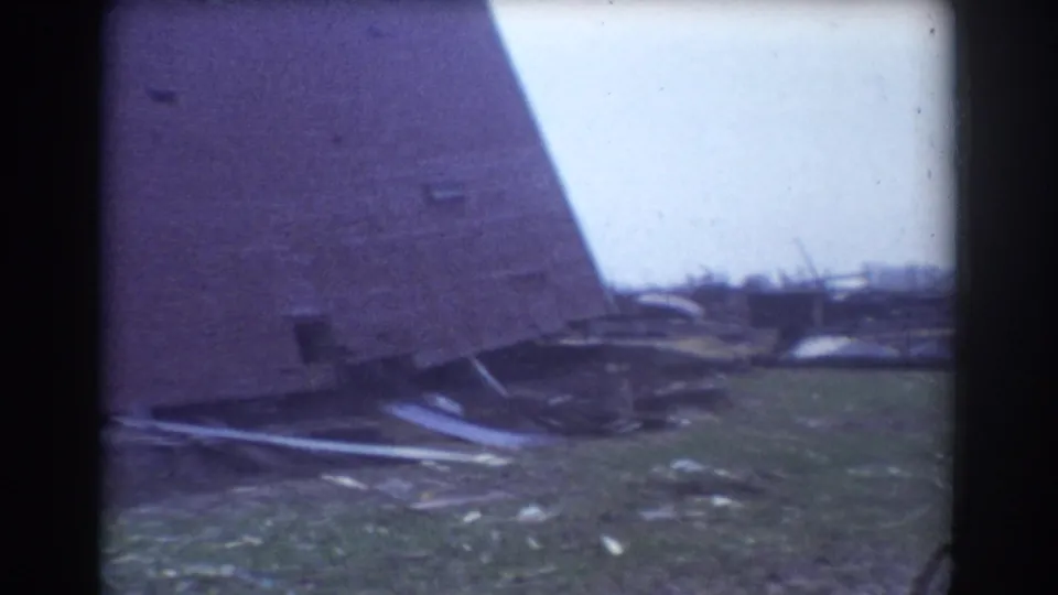 1958 York, Nebraska home-movie frame showing the side of a damaged structure and storm debris scattered across grass.