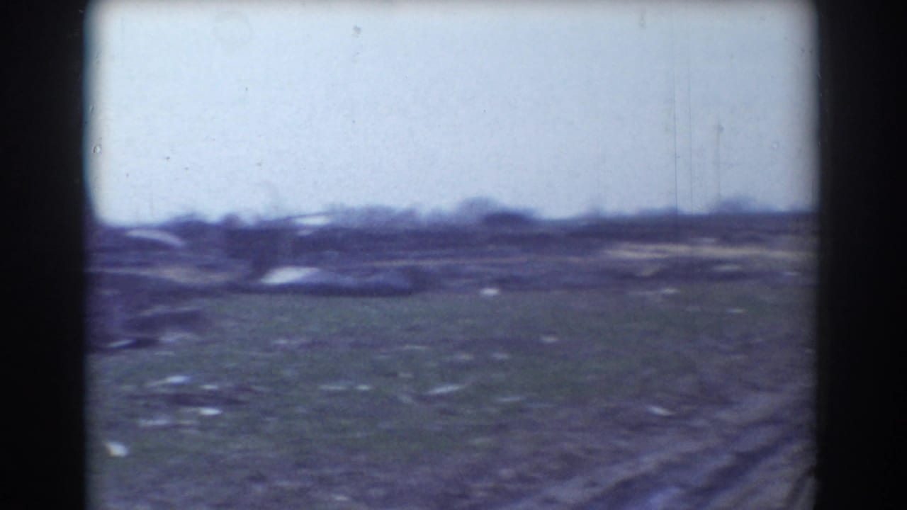 1958 York, Nebraska 8mm frame showing a muddy open field, scattered debris, and low damaged material on the horizon.