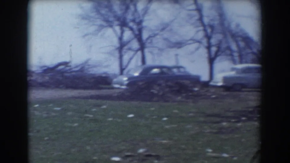 1958 York, Nebraska 8mm frame showing parked 1950s cars near bare roadside trees and debris on grassy ground.