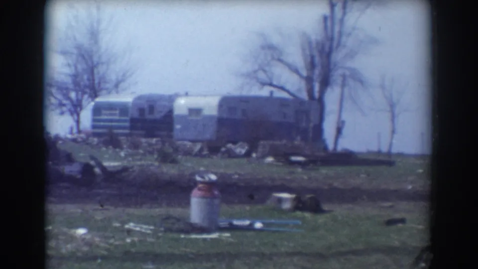 1958 York, Nebraska frame with trailers or mobile homes behind a grassy yard, a milk can, scattered objects, and leafless trees.