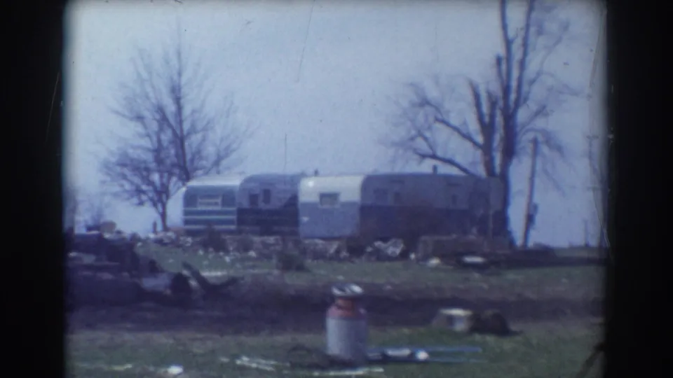 1958 York, Nebraska 8mm frame showing several trailers, bare trees, a milk can, logs, and scattered debris in a rural yard.