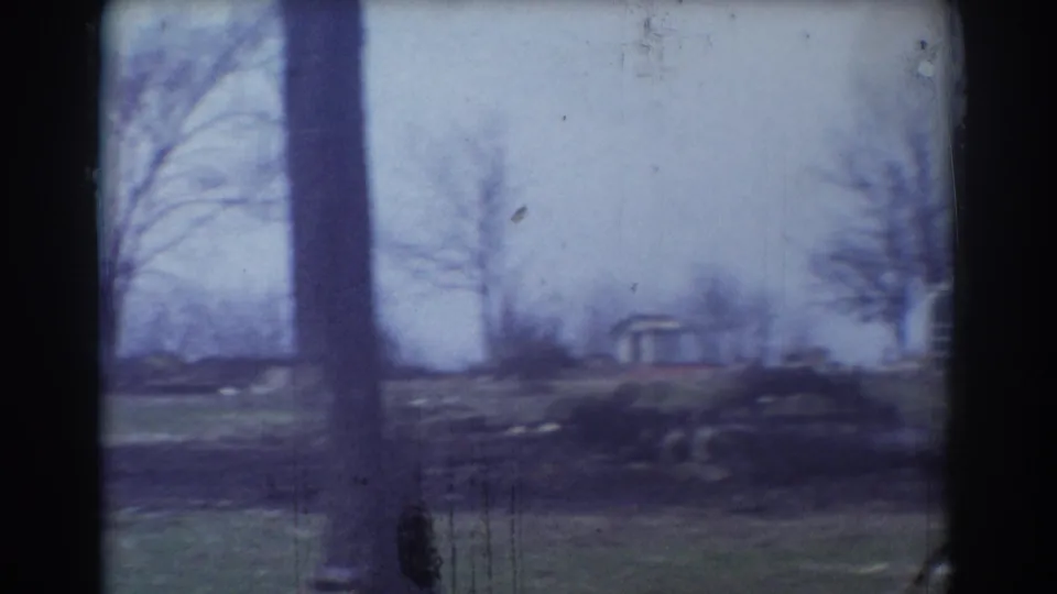 1958 8mm view in York, Nebraska, showing bare trees, open grass, and a small distant structure under a pale sky.