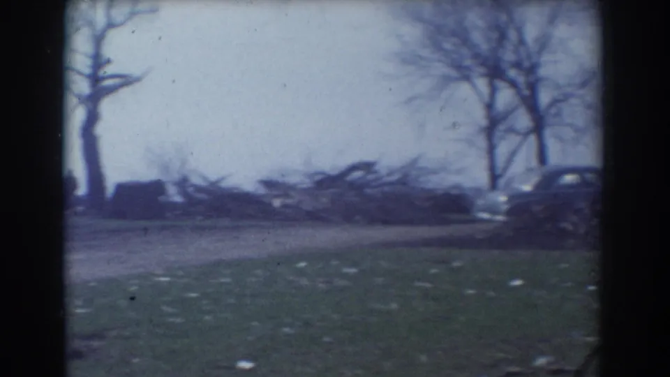 Soft 8mm frame of a roadside area in York, Nebraska, with leafless trees, scattered debris, grass, and parked cars at the edges.