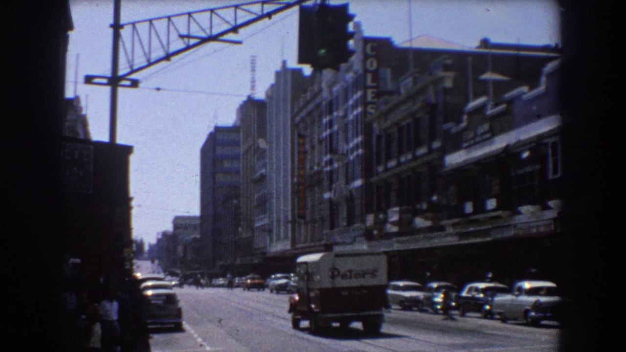 Downtown street with traffic, pedestrians, a delivery truck, and shopfront signs.