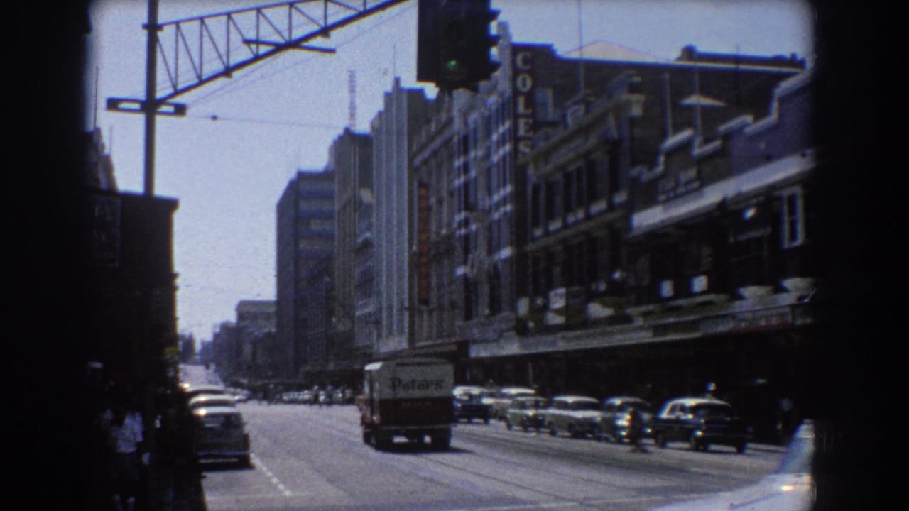 City street with cars, pedestrians, overhead signal, and vertical shop signage.