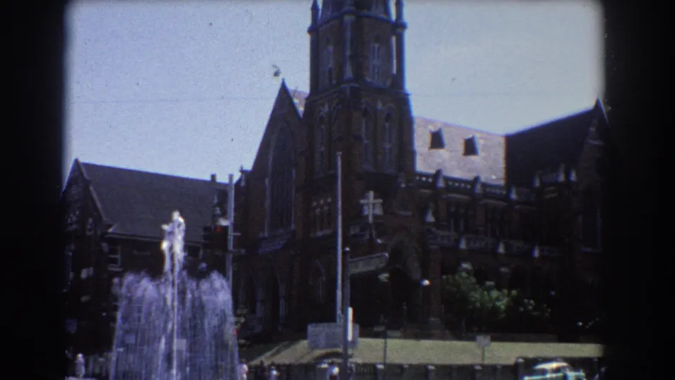 1967 Brisbane public fountain viewed before a large brick church exterior, with cars and pedestrians nearby.