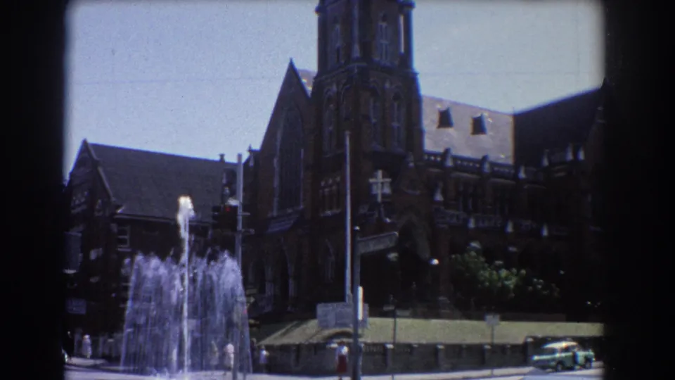 1967 Brisbane fountain and brick church exterior with pedestrians and cars along the surrounding street.