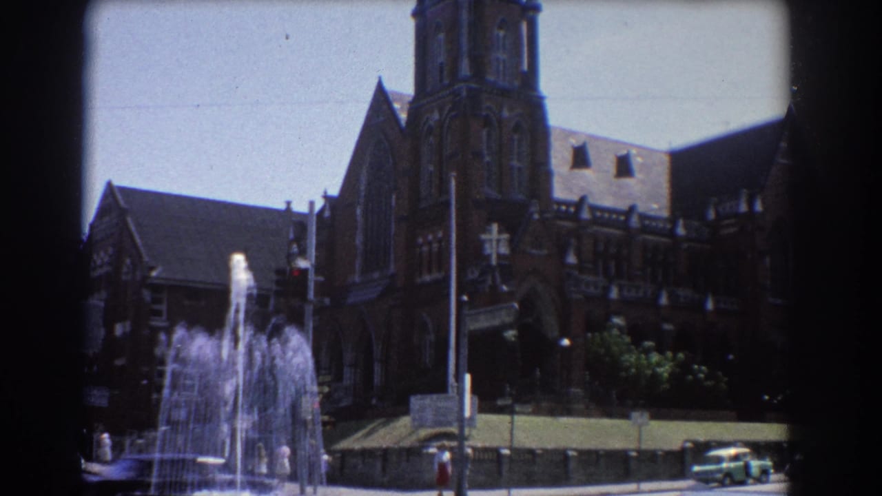 Water fountain in front of a large brown brick cathedral-like building on a sunny street.