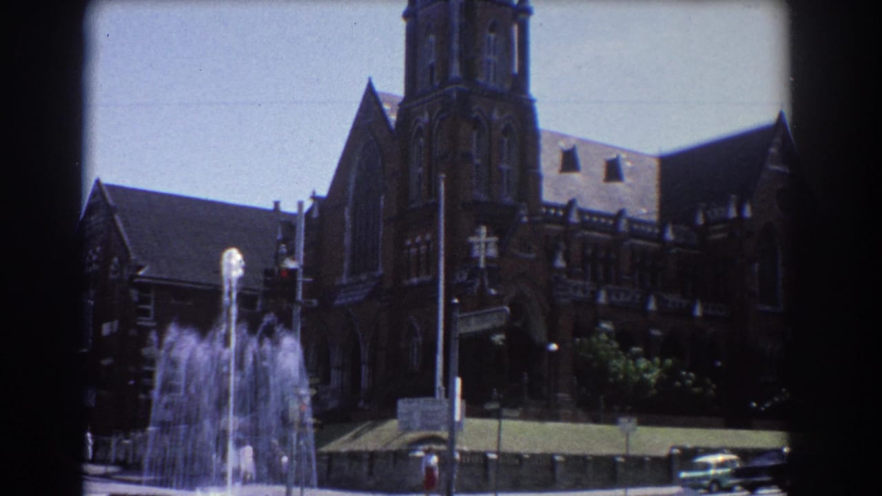 Fountain and brown brick cathedral-like building seen from across a sunny street.