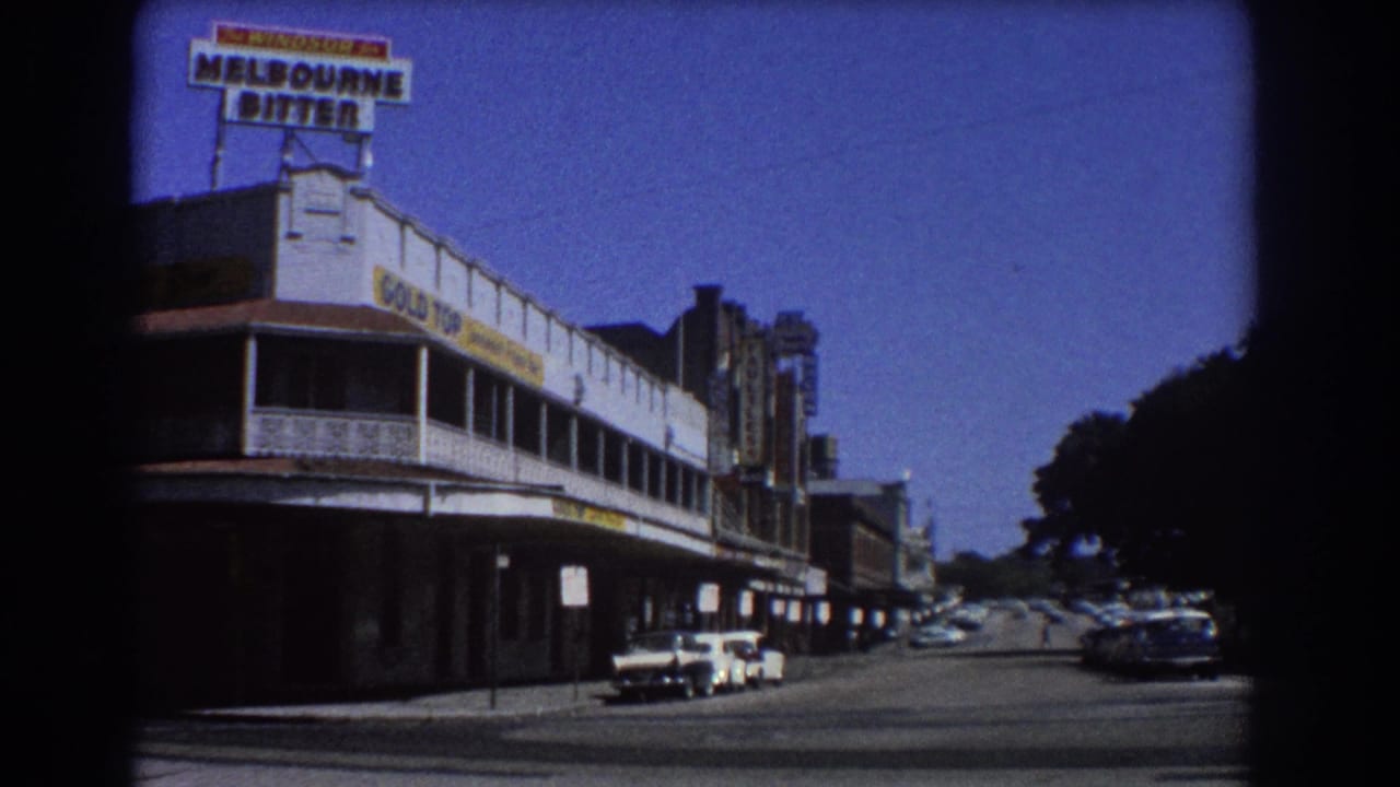 Similar street-corner view with rooftop beer sign, long awning, parked cars, and shaded trees at right.