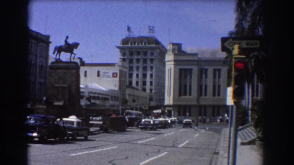 1967 Brisbane intersection view with an equestrian statue at left, mid-century cars, a red traffic light, and a one-way street sign.