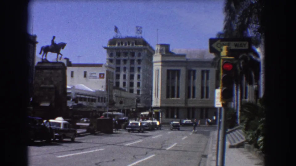 1967 Brisbane city intersection with an equestrian statue, roadway traffic, public buildings, and a red signal beside a one-way sign.