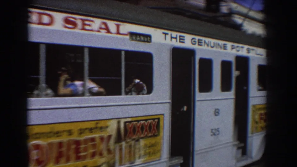 1967 Brisbane street tram seen close from the side, with passengers in windows and alcohol advertising along the exterior.