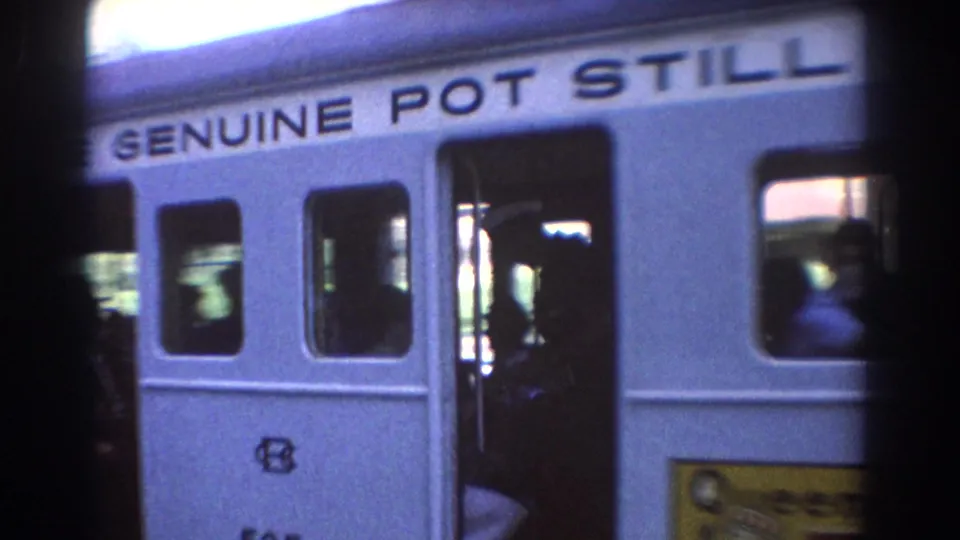 White Brisbane tram in 1967, viewed through a dark obstruction, with open doors, passengers, and pot still advertising text.
