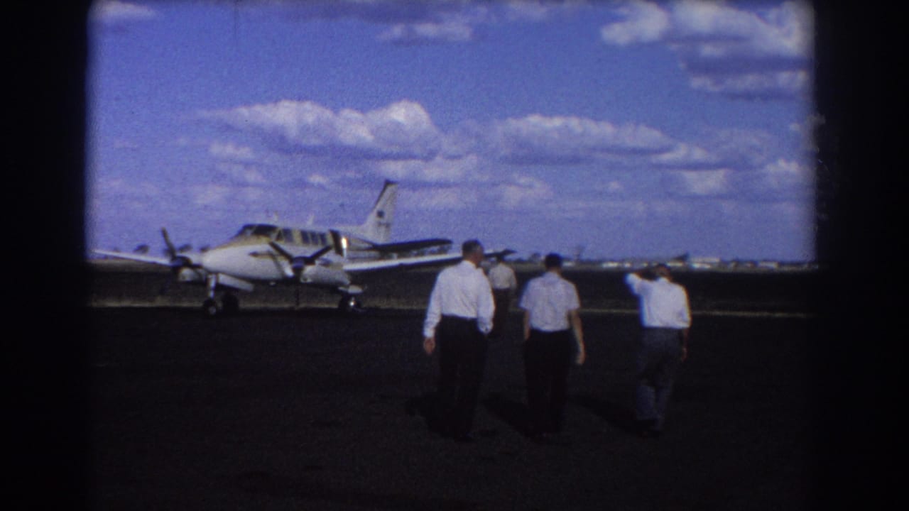 Men continue toward a parked twin-engine plane with its nose and wing visible on the tarmac.