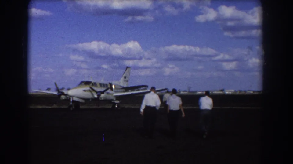 Brisbane, Australia, 1967 home-movie frame shows three men approaching a small twin-engine propeller plane on the tarmac.