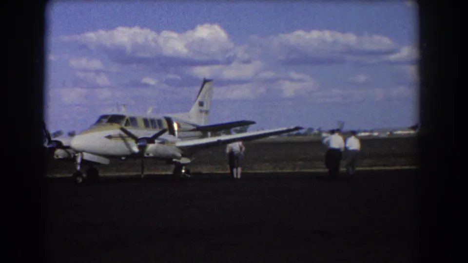 1967 Brisbane frame showing a closer view of a small twin-engine plane with men gathered near the right wing.