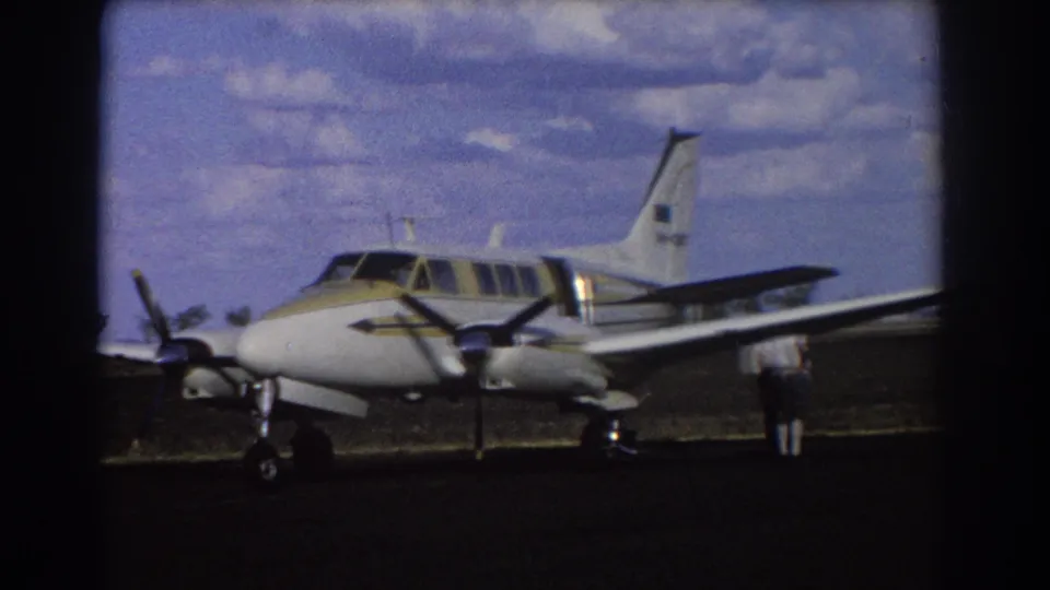 1967 Brisbane 8mm frame with the small aircraft filling the view and a man standing near the wing on the airfield.
