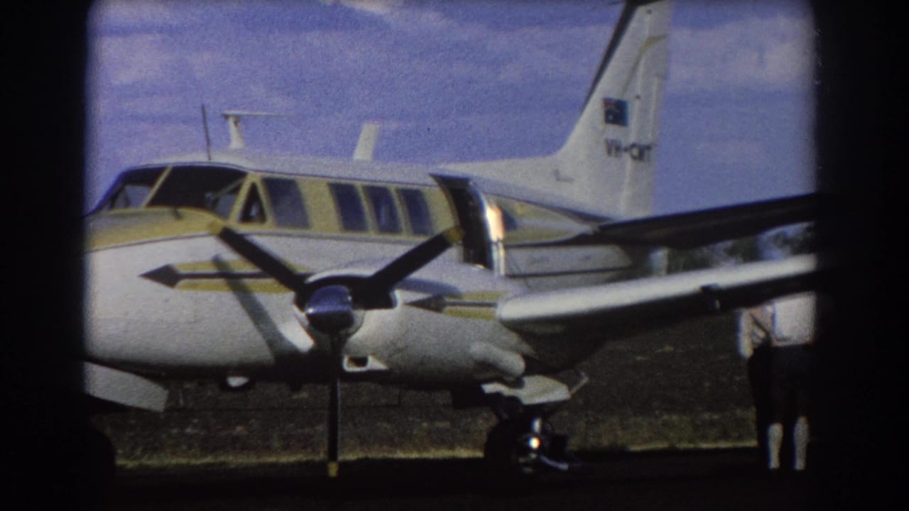 Closer view of a white and yellow propeller airplane with tail markings on a sunny airfield.