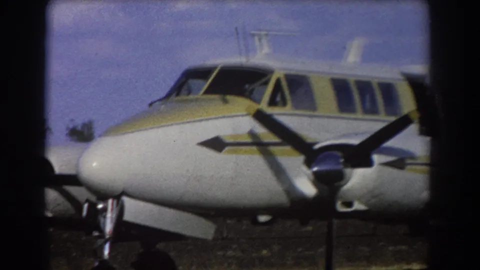 Close 1967 Brisbane home-movie view of the airplane nose, cabin windows, yellow livery, and dark propeller blade.