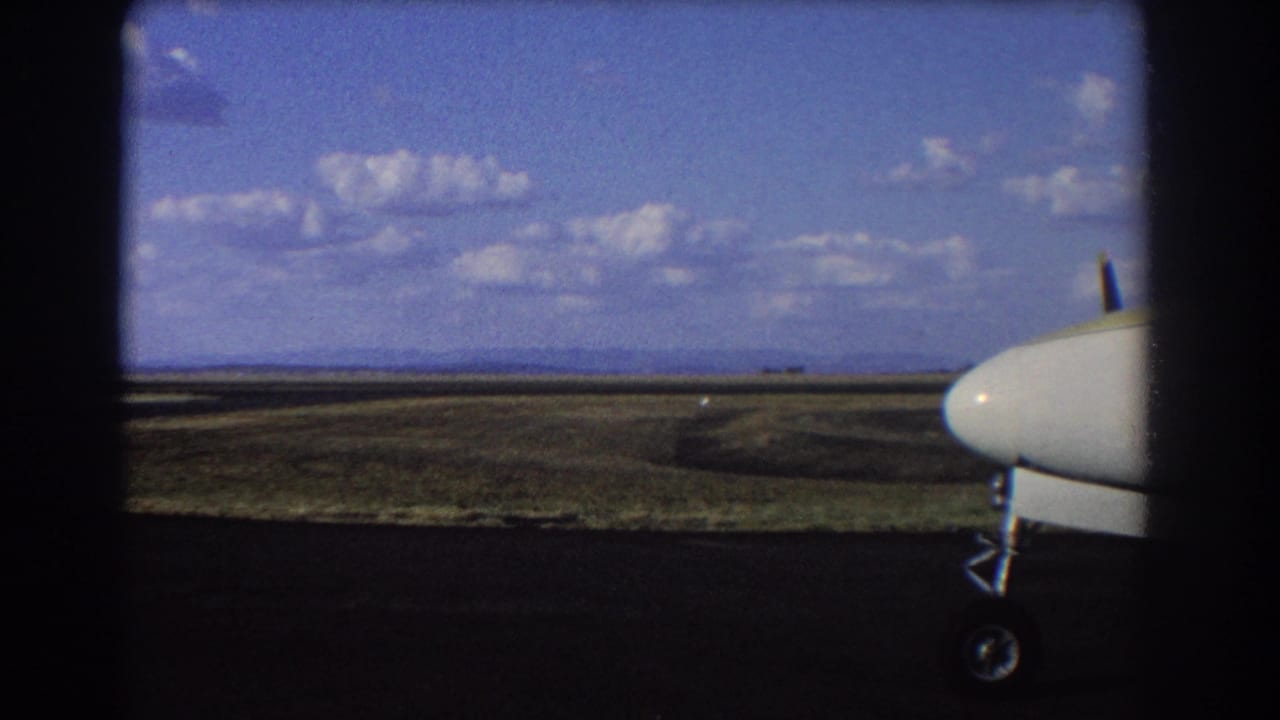 Small aircraft nose and landing gear beside an open runway landscape under a blue sky.